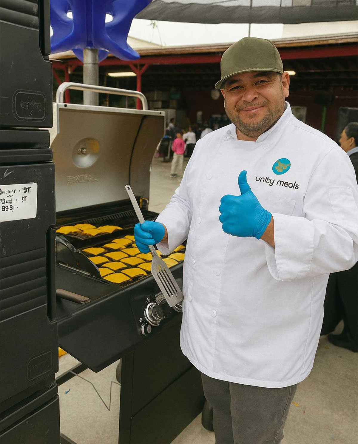 Unity Meals chef smiling at the camera while cooking burgers on an outdoor grill