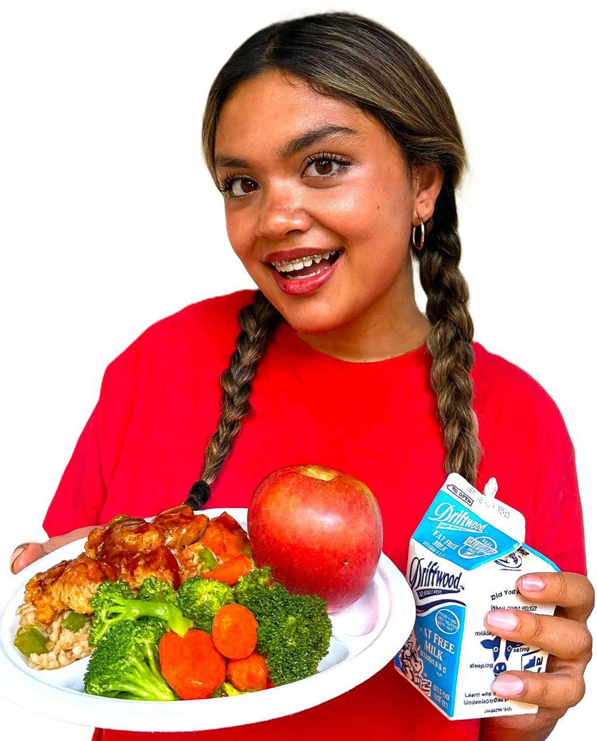 Young girl in a red shirt holding a plate of chicken with an apple and side of mixed vegetables and also holding a carton of milk